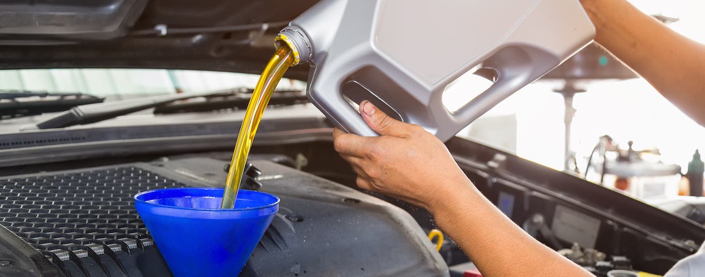 A mechanic is pouring oil into a blue funnel and into a car as part of an oil change service.
