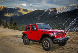 Jeep Wrangler driving on dirt road by mountains