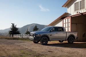 Ram truck parked in front of a barn with a forest and mountains in the background