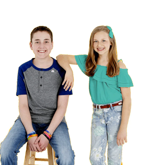 A smiling pre-teen girl leaning on the shoulder of a similarly aged boy with silicone bands on his wrists.