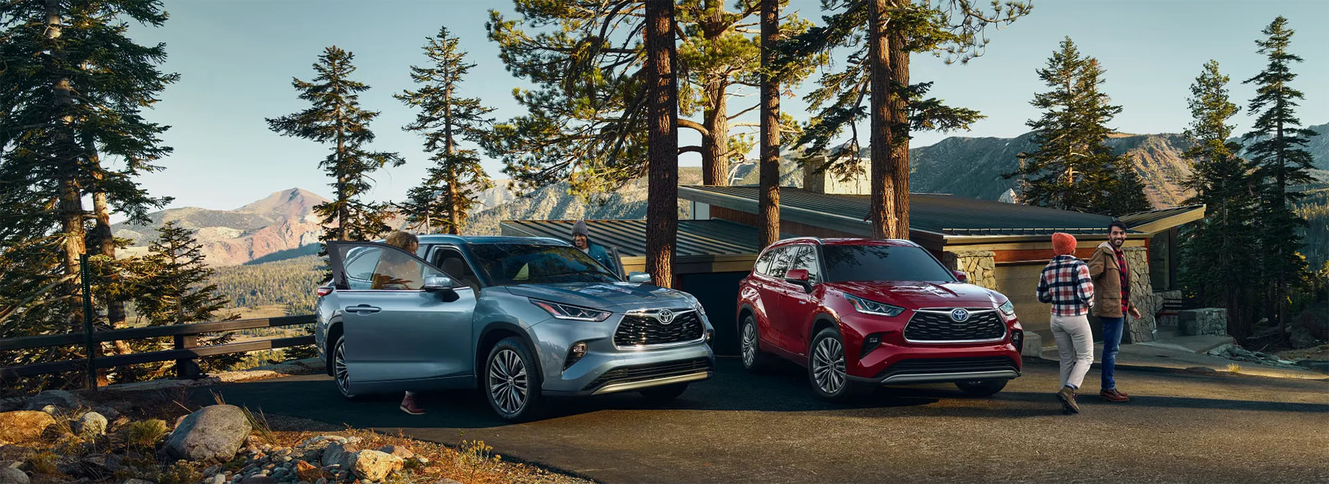 Highlander Platinum shown in Moon Dust and Highlander Platinum Hybrid shown in Ruby Flare Pearl parked at a house in the mountains.