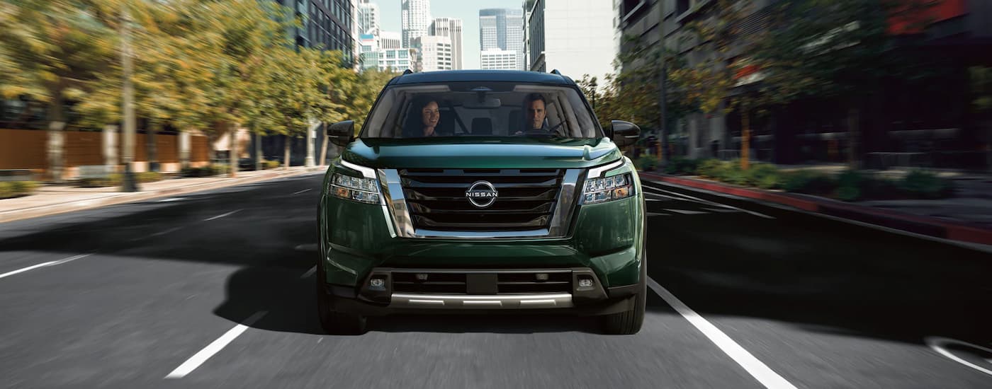 Front view of a couple driving through the city in a green 2022 Nissan Pathfinder