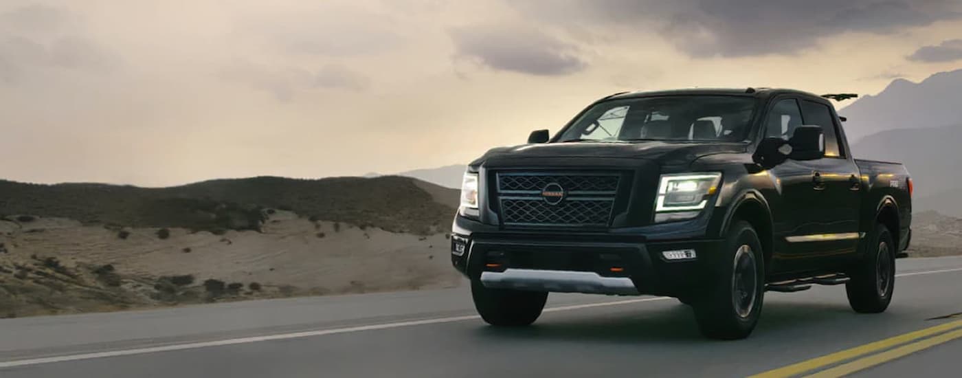 A black 2022 Nissan Titan driving on an open highway past hills and mountains