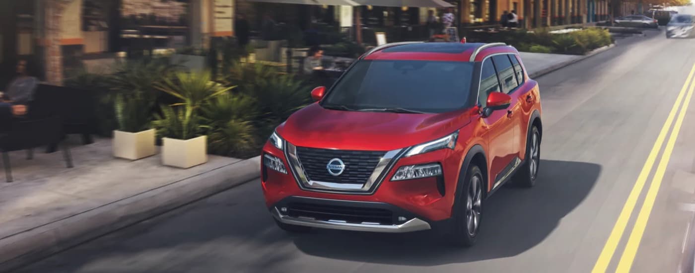 A red 2022 Nissan Rogue is shown driving on a city street.