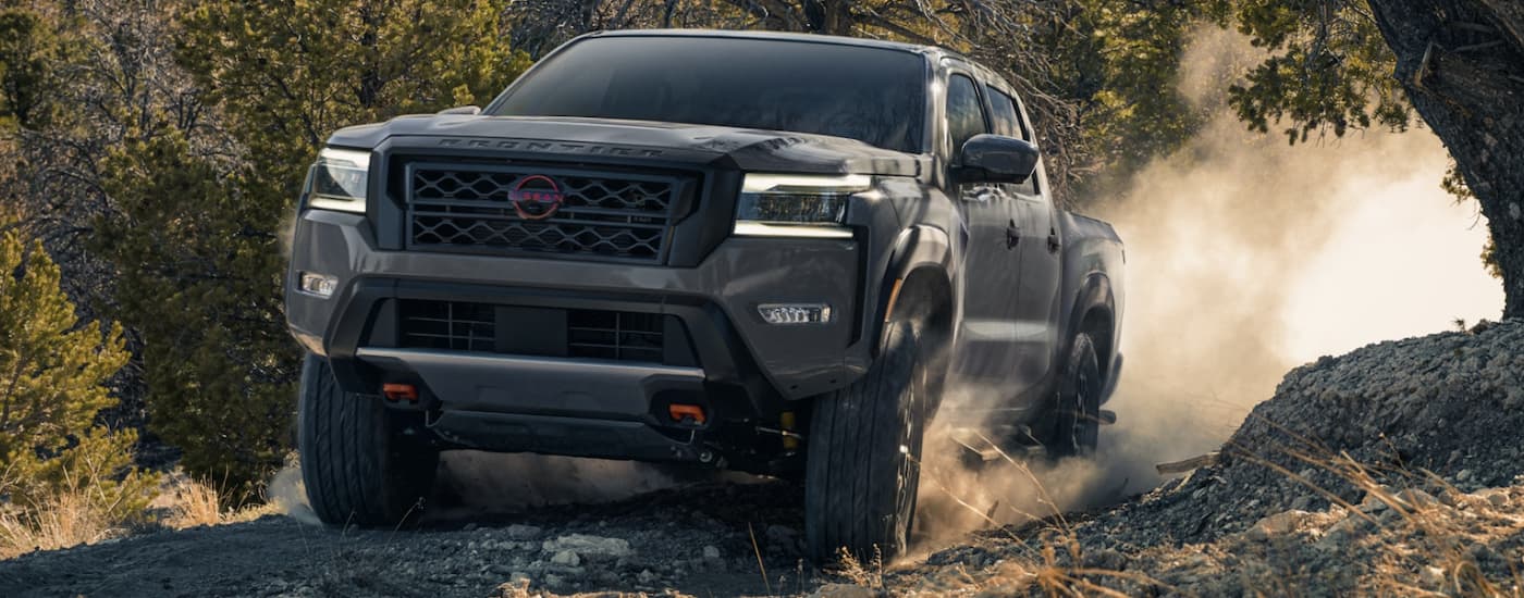 Front view of a dark grey 2022 Nissan Frontier driving up a dusty dirt path