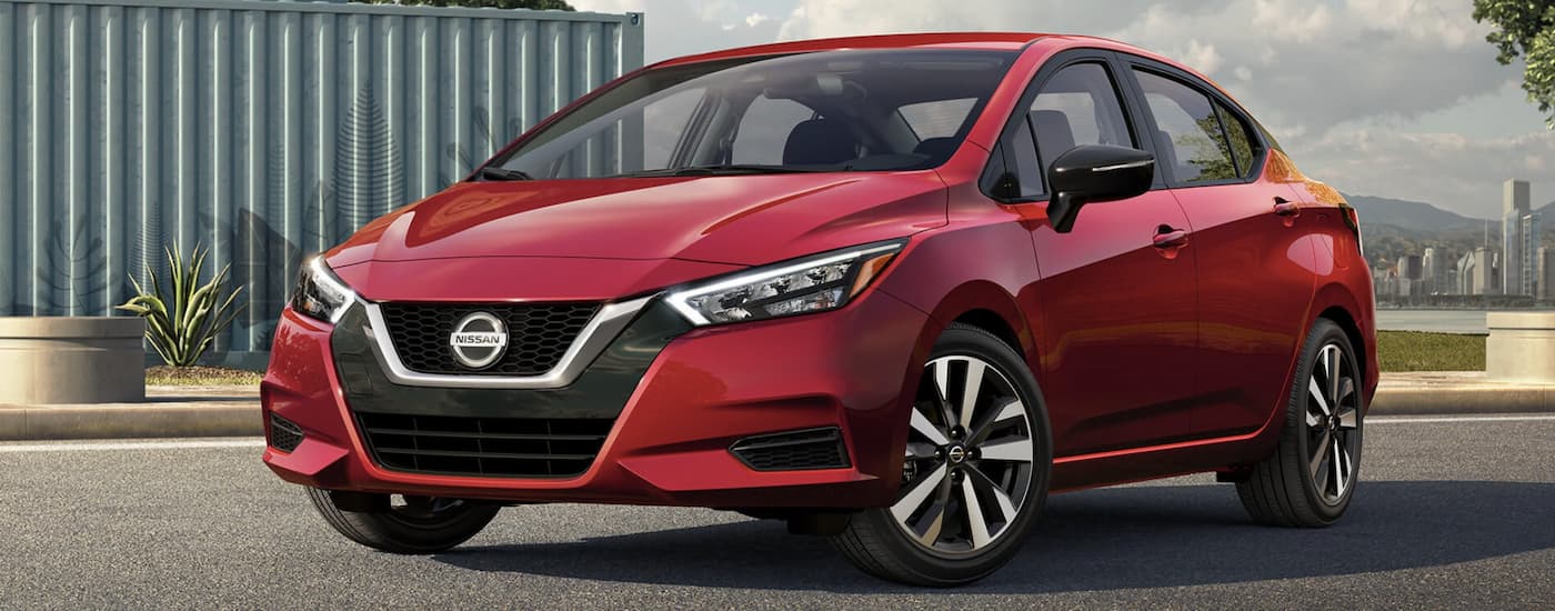 Red 2022 Nissan Versa parked by an industrial building in front of a city