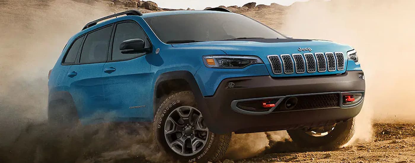 A blue 2022 Jeep Cherokee Trailhawk is shown off-roading on a dusty trail.