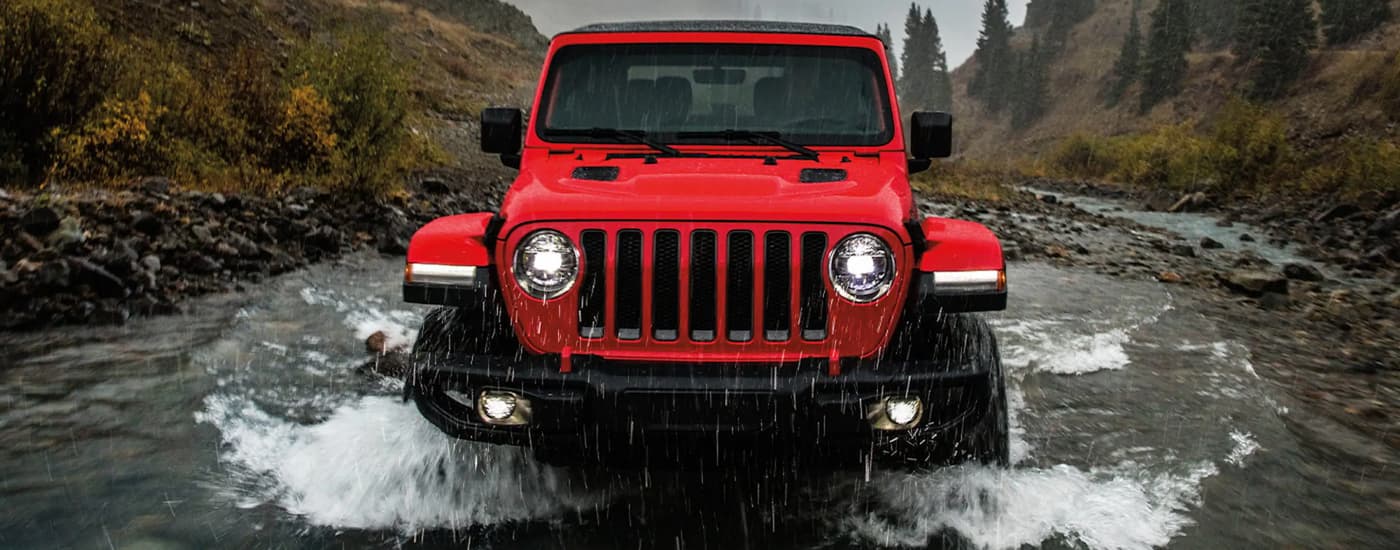A red 2022 Jeep Wrangler Rubicon is shown driving through a river.