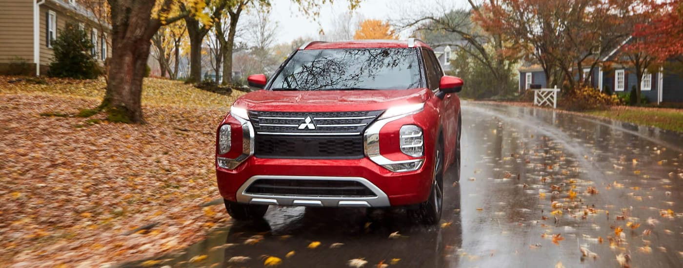 A red 2022 Mitsubishi Outlander is shown from the front driving on a wet autumn road.