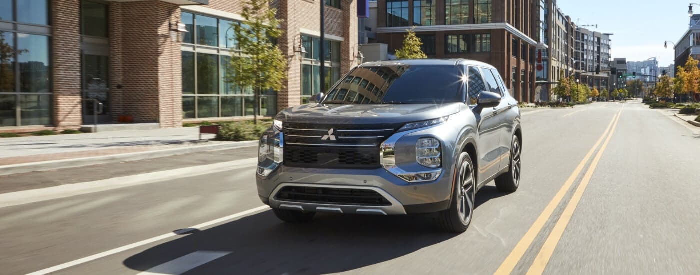 A grey 2022 Mitsubishi Outlander is shown driving on a city street.