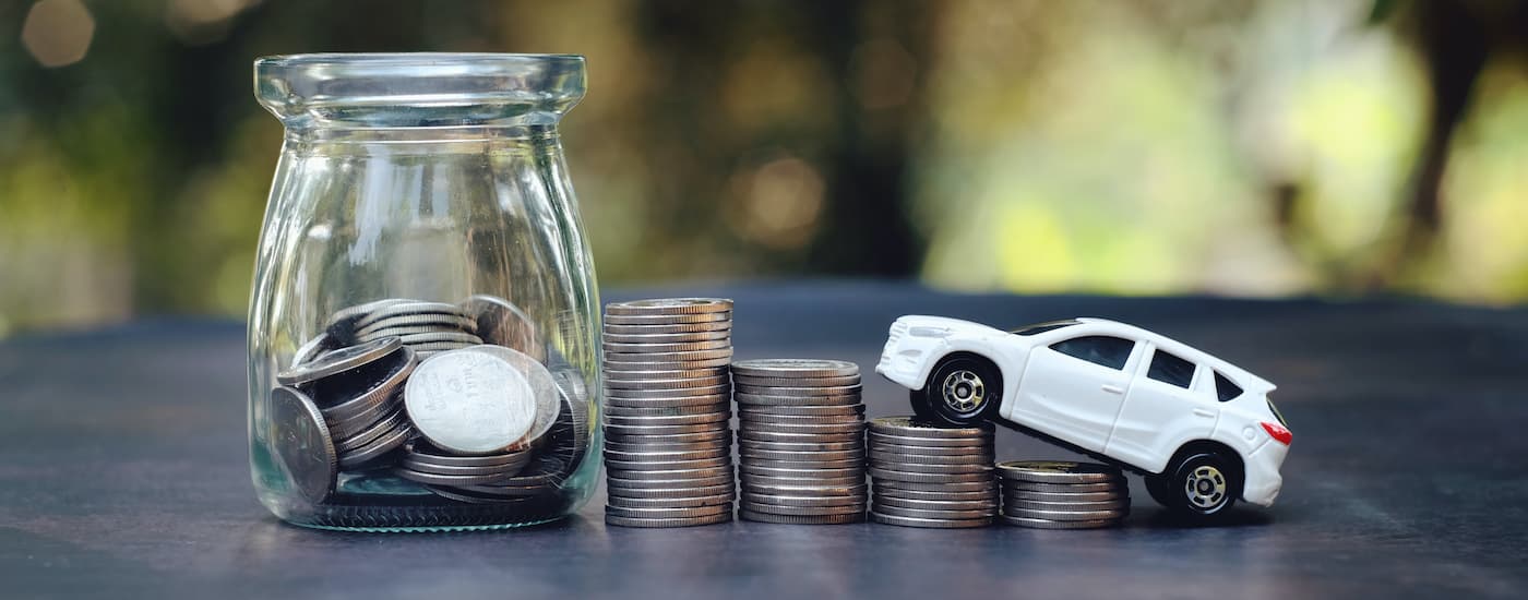 White toy SUV heading up four stacks of coins toward a jar of coins