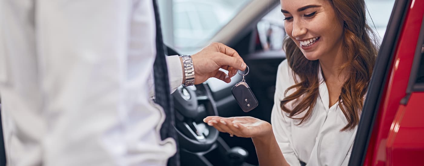 Car salesman handing keys to a smiling woman in a red car