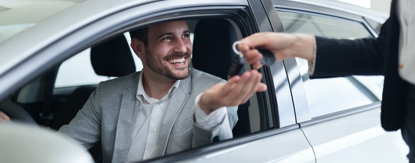 Car salesman handing a smiling customer keys to the new car he is sitting in