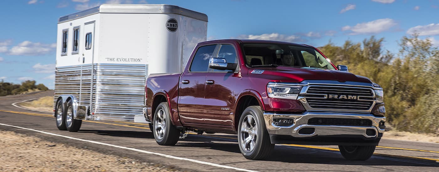 A red 2022 Ram 1500 Laramie is shown towing a horse trailer.