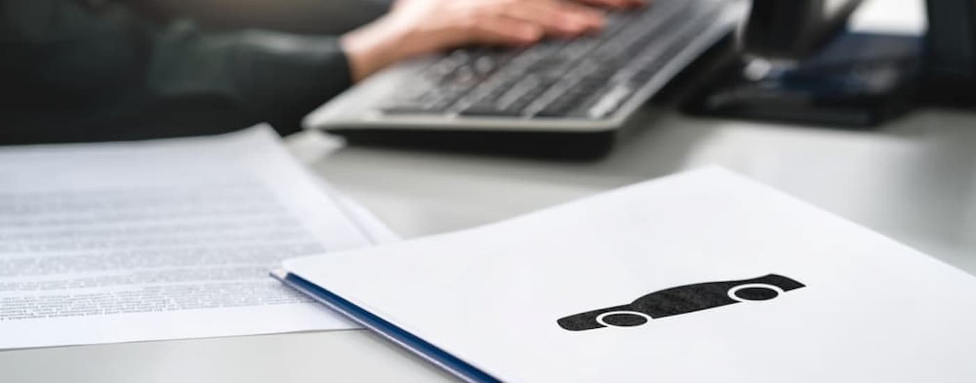 A vehicle salesperson typing on a computer keyboard with papers in front of him