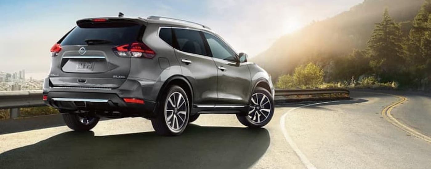 Side view of a grey 2018 Nissan Rogue pulled over at a lookout point in front of the city