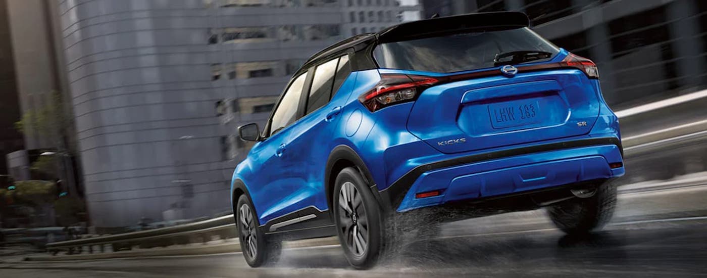 Back view of a blue 2021 Nissan Kicks driving on a city-side highway