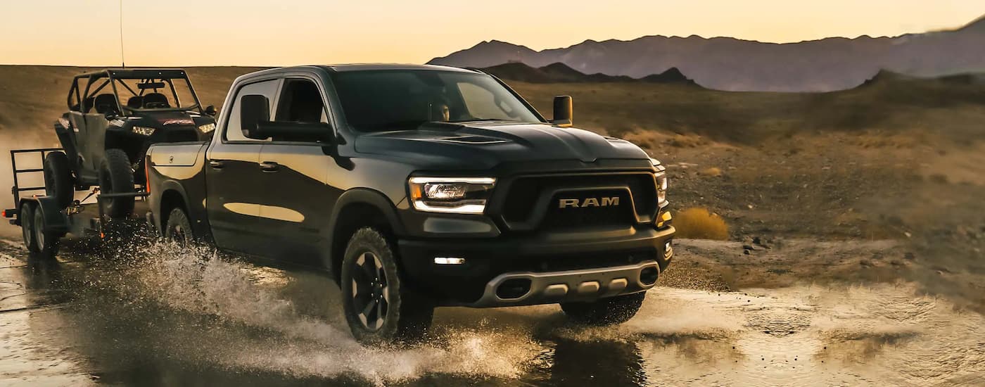 A black 2022 Ram 1500 is shown towing an ATV through water.