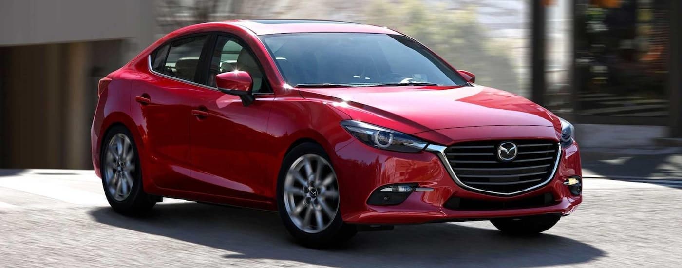 A red 2018 Mazda3 is shown rounding a corner on a city street.