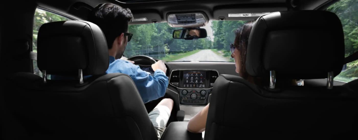 A couple is shown driving a 2022 Jeep Grand Cherokee WK on a forest road.