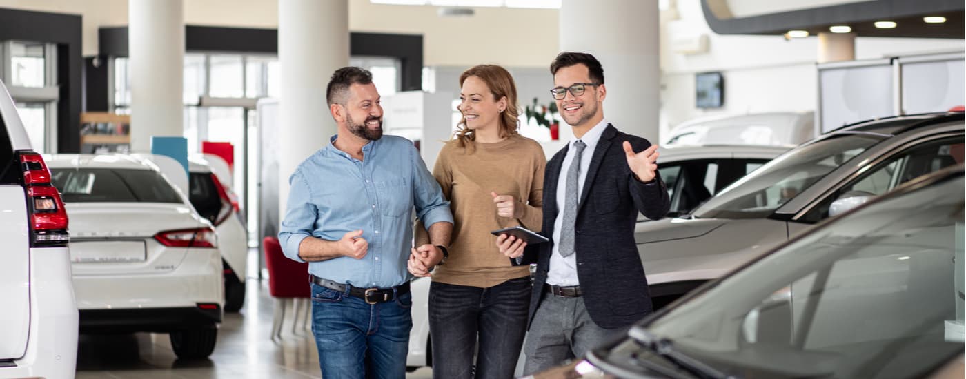 Car salesman walking through the vehicle showroom with a couple