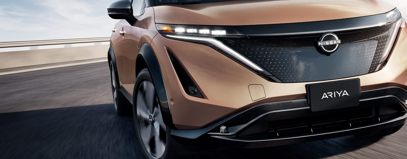 Front grille view of a brown 2023 Nissan Ariya driving to a Nissan Dealer near you