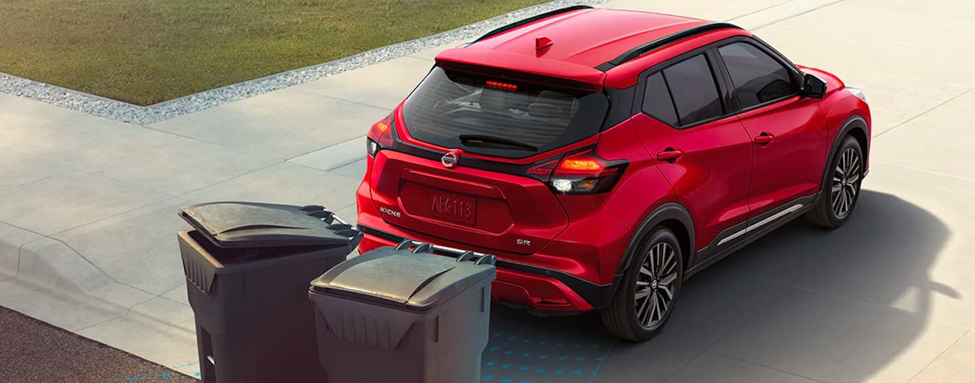 A red 2021 Nissan Kicks SR backing toward garbage cans in a driveway