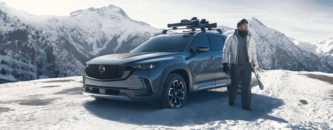 Man standing next to a grey 2023 Mazda CX-50 in the snowy mountains