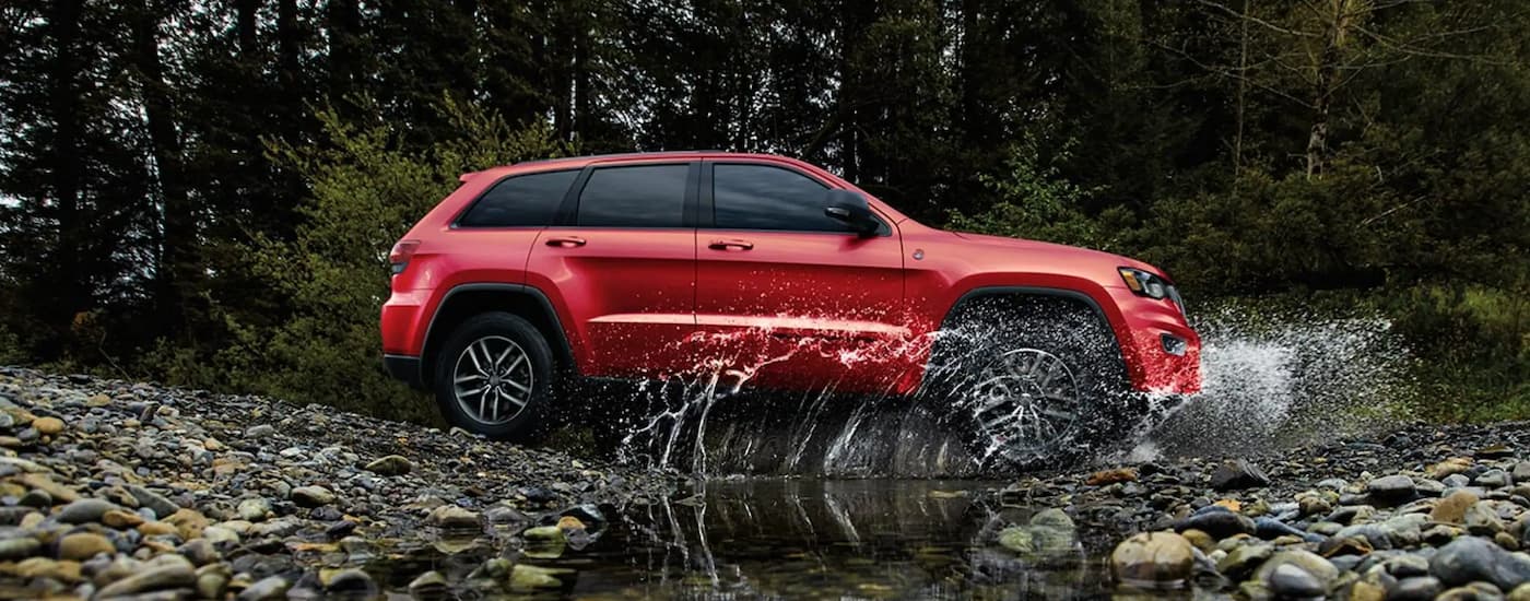 A red 2020 Jeep Grand Cherokee is shown from the side driving through a small brook.