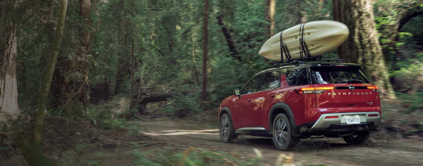 Red 2022 Nissan Pathfinder with a kayak on the roof driving through the woods
