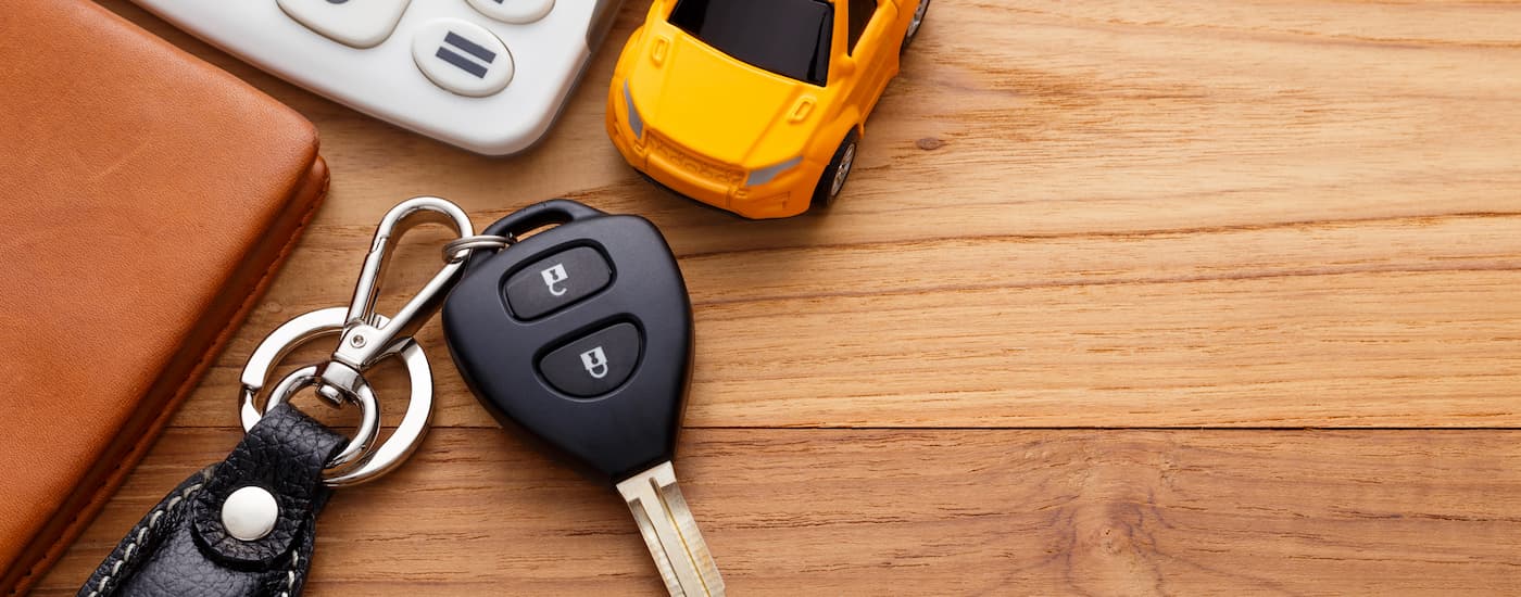 Car key, yellow toy car, and calculator sitting on a brown wooden desk