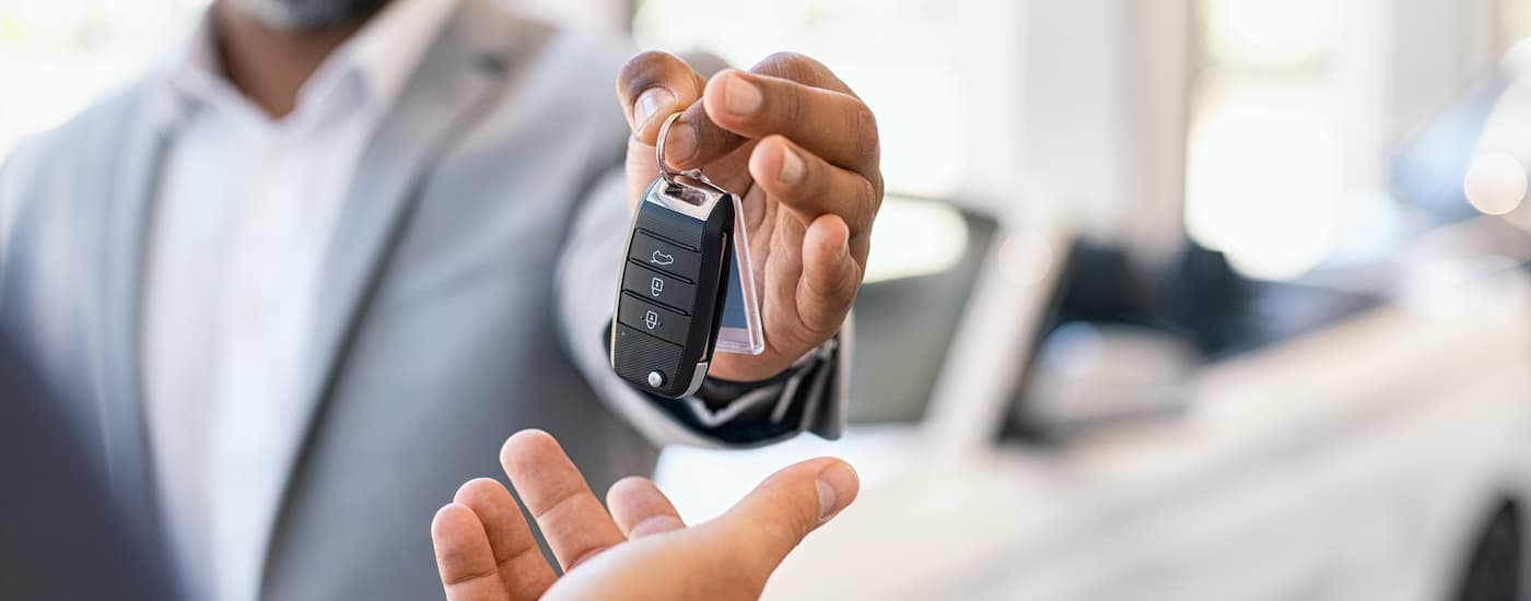 Car salesman in a grey suit handing over car keys to a customer