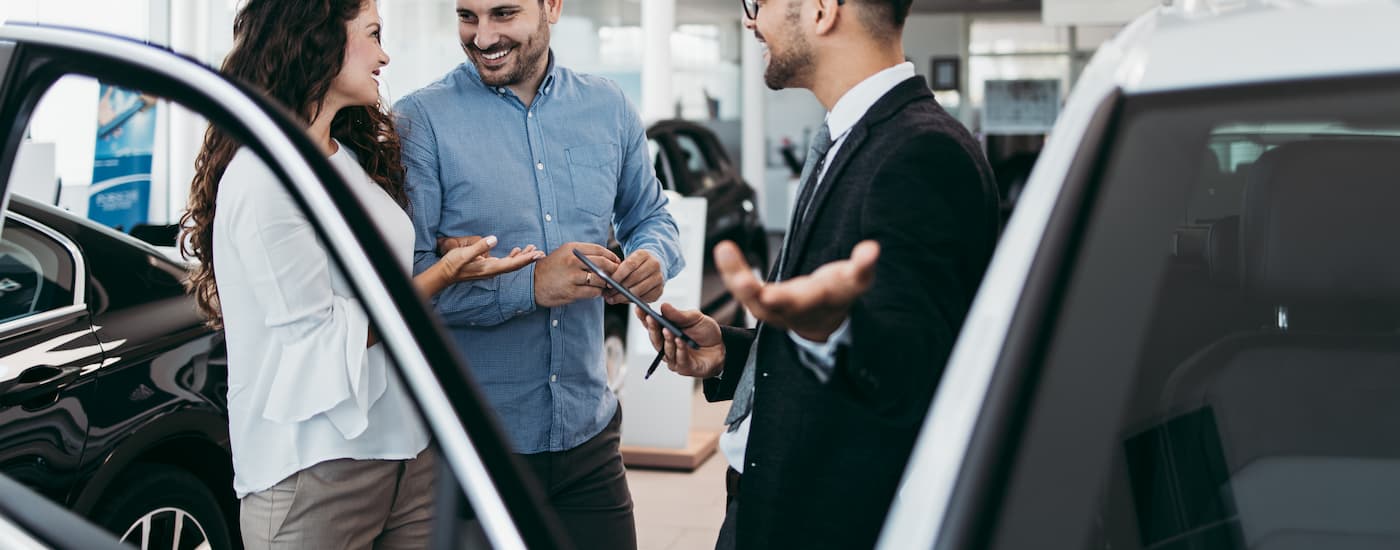Man in a vehicle showroom discussing auto loans with a couple