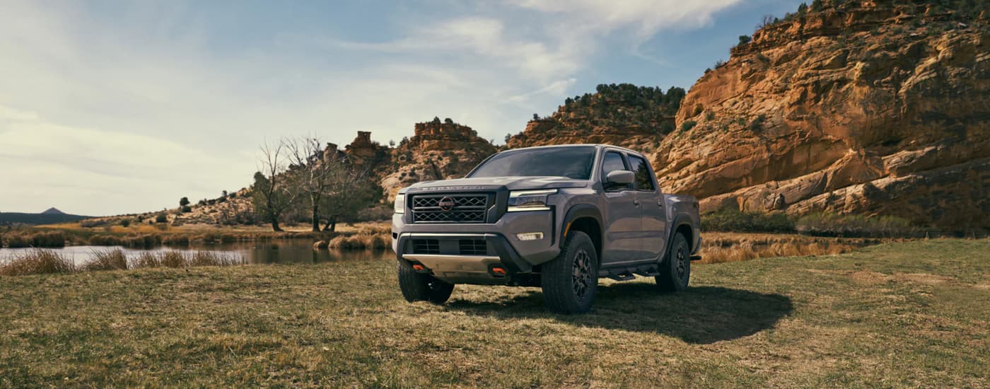 A grey 2022 Nissan Frontier Pro-4x parked in a grassy field by a pond and rocky hills