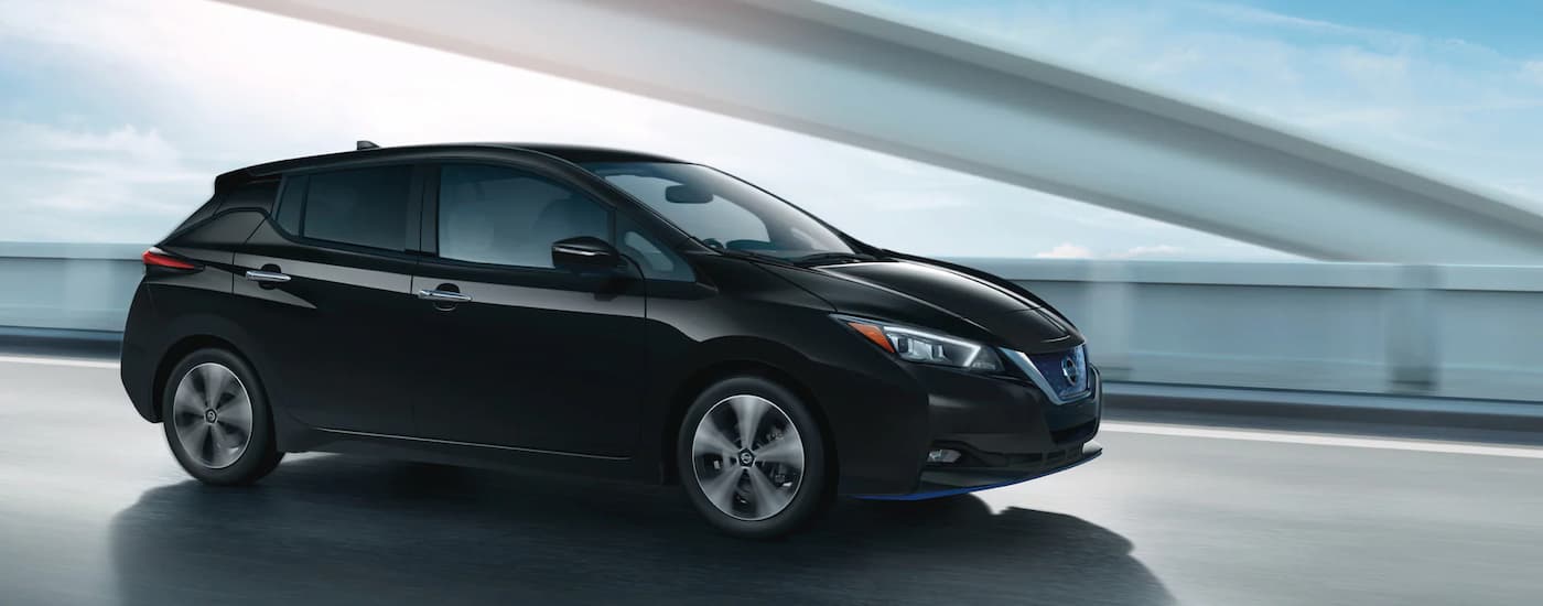Side view of a black 2022 Nissan Leaf driving over a bridge