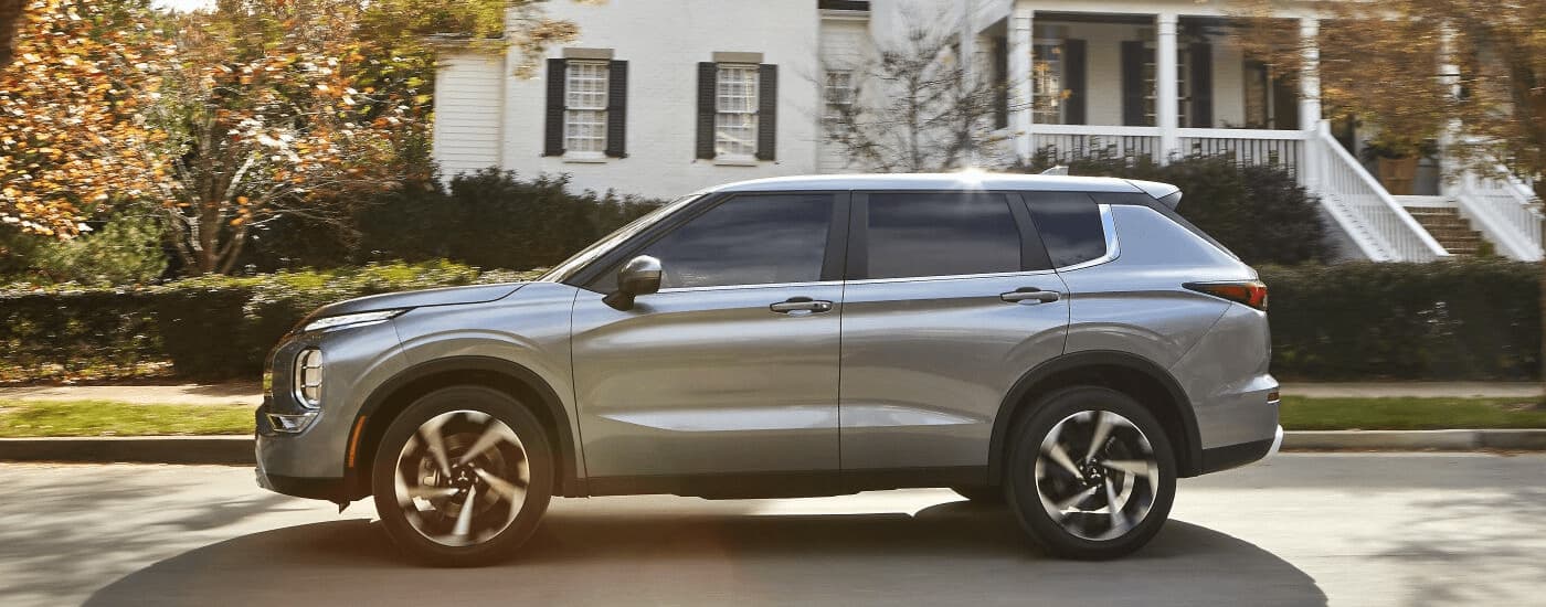 A silver 2022 Mitsubishi Outlander is shown from the side driving through a neighborhood.