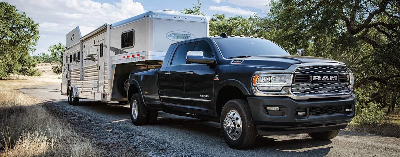 A black 2019 Ram 3500 is shown towing a camper trailer towards a campsite.
