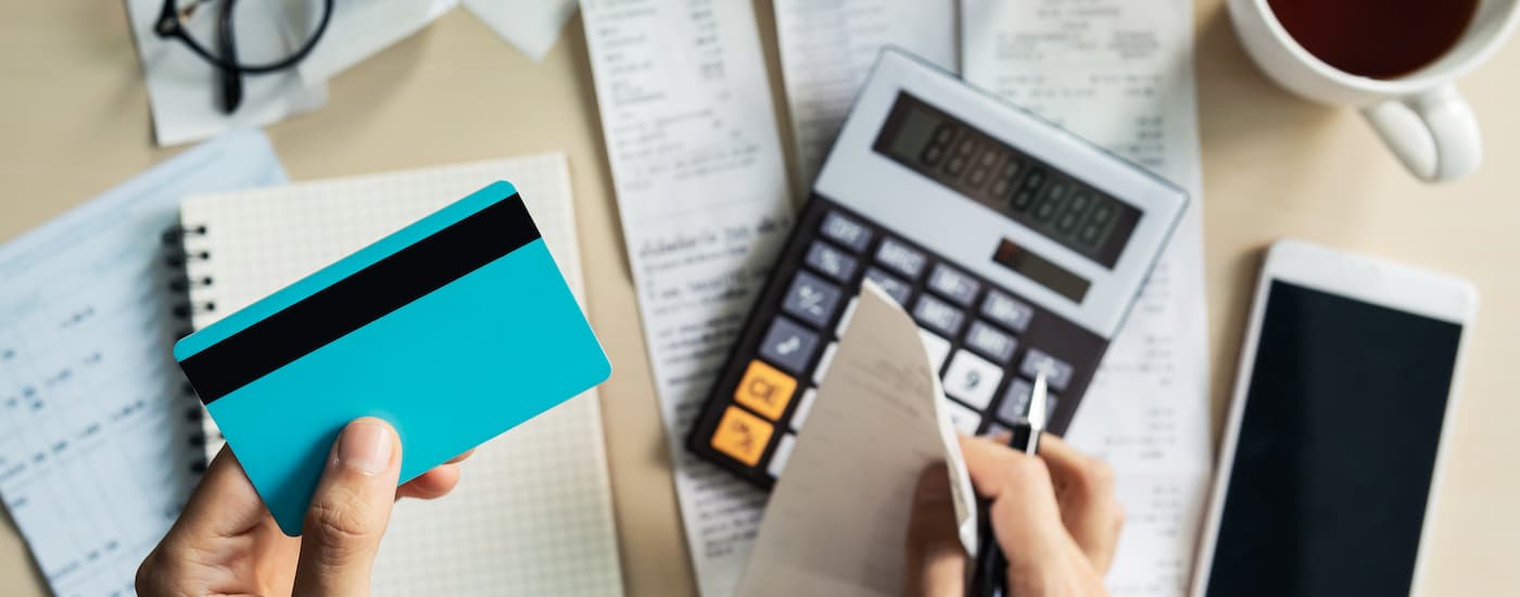 Hand holding a blue credit card above a table filled with receipts and a calculator