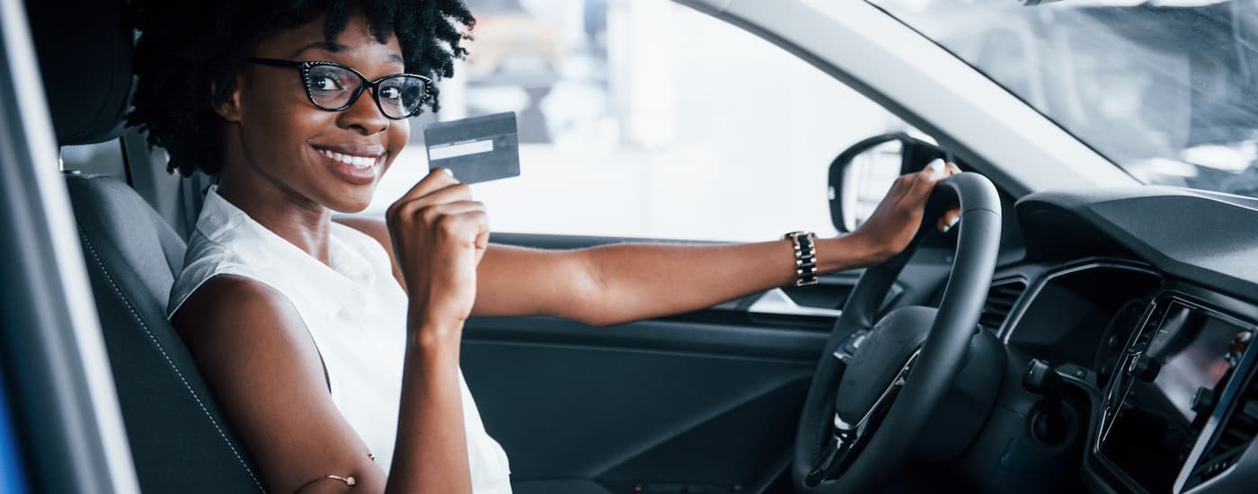 Woman smiling with a credit card in the driver's seat of a new vehicle