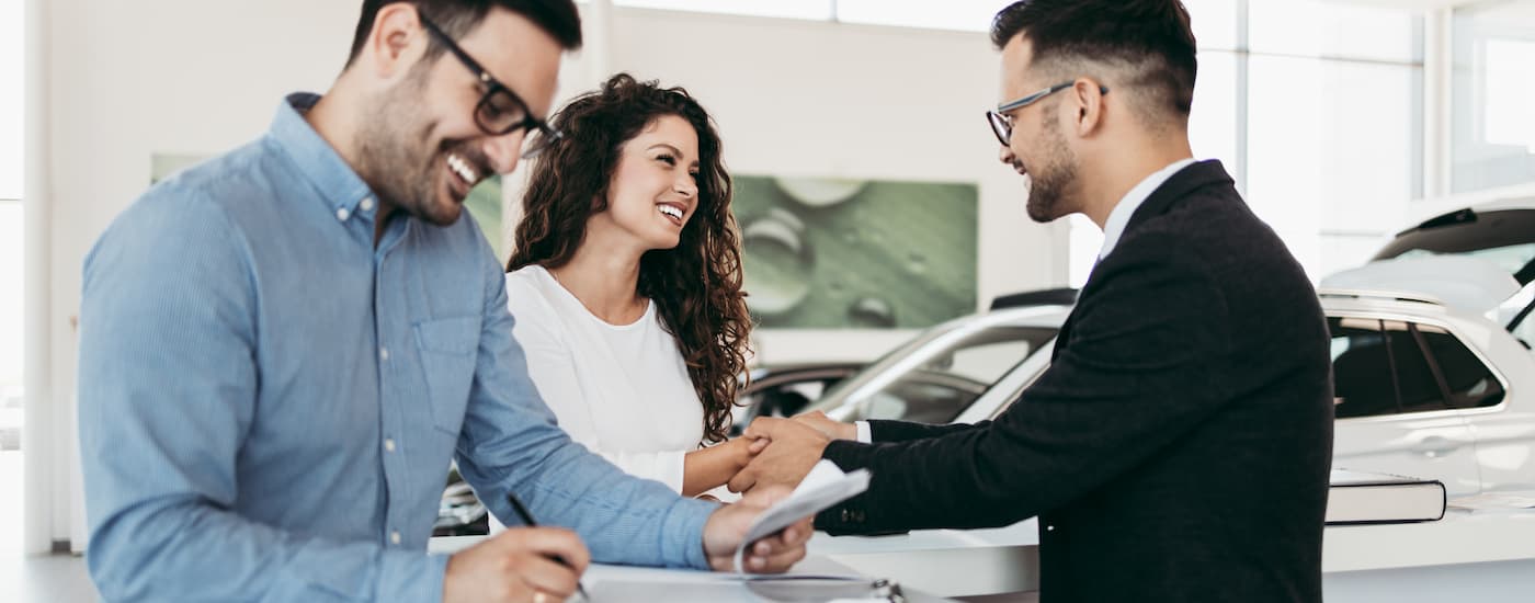 Man shaking hands with a woman while her husband signs auto loan paperwork