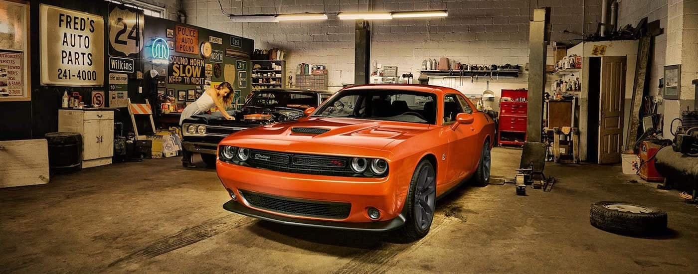 An orange 2019 Dodge Challenger is shown parked near a two post lift in a garage.