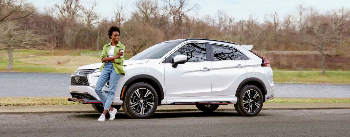 A woman is shown standing near the front of a white 2022 Mitsubishi Eclipse Cross.