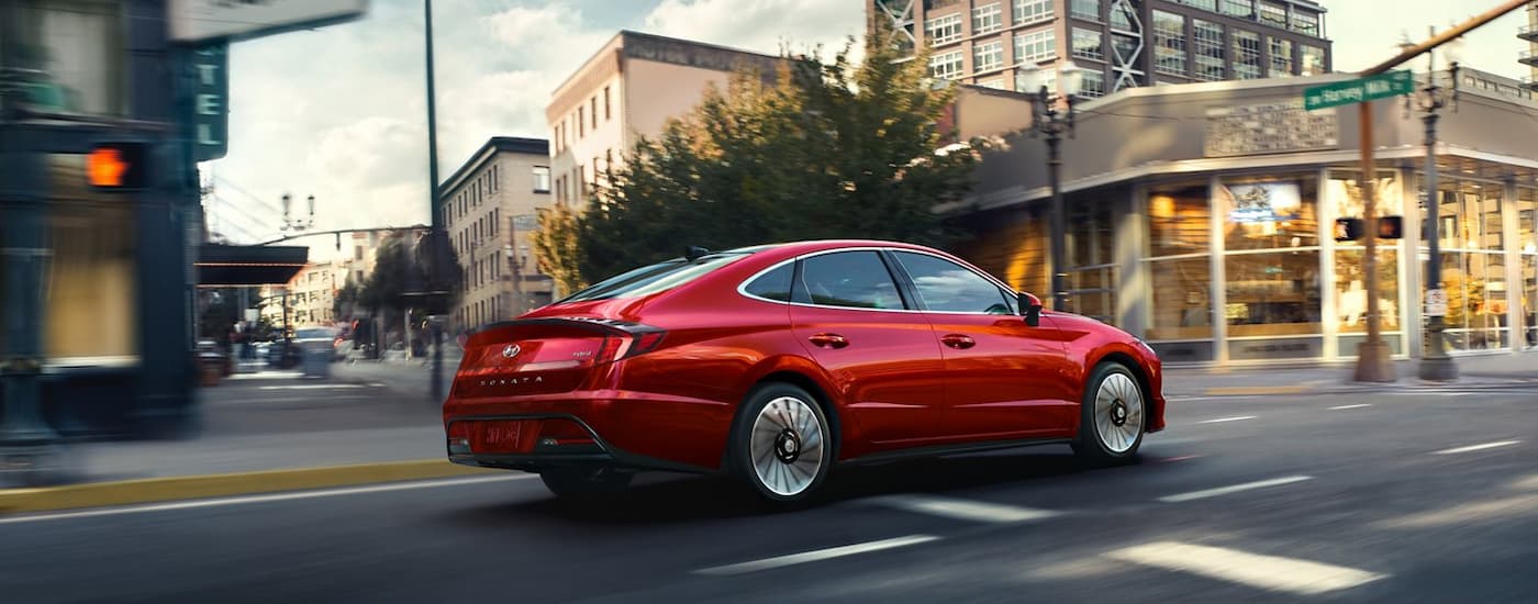 A red 2022 Hyundai Sonata Hybrid driving through city streets near a Hyundai dealership in Alberta