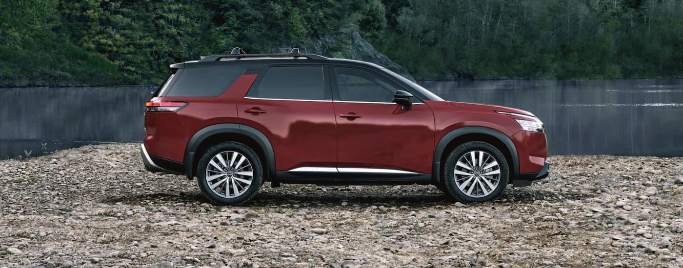 A red 2022 Nissan Pathfinder parked in gravel next to a pond