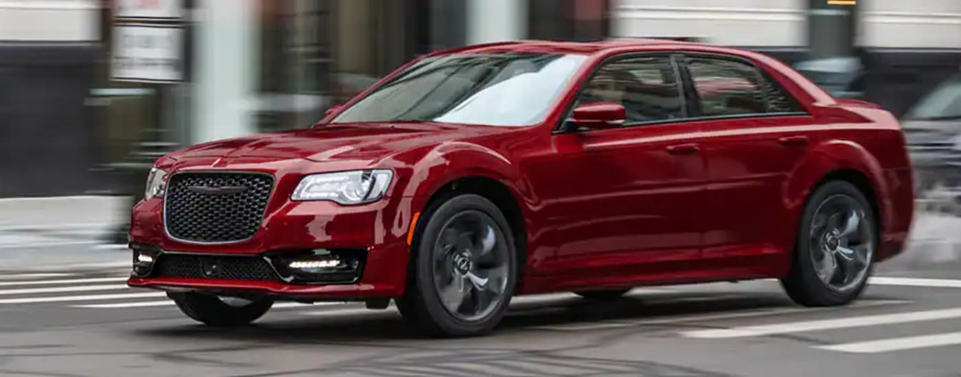 A red 2021 Chrysler 300 is shown from the side driving through a city after leaving a used Chrysler dealer.
