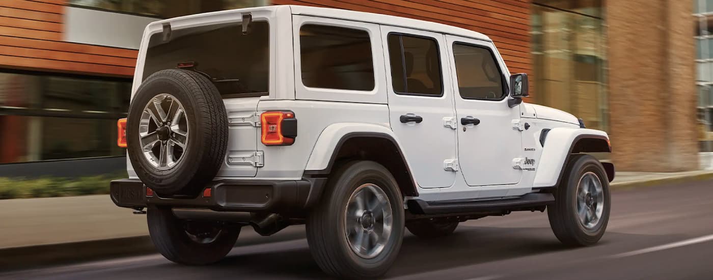 A white 2022 Jeep Wrangler Sahara Unlimited is shown from the rear driving through a city.