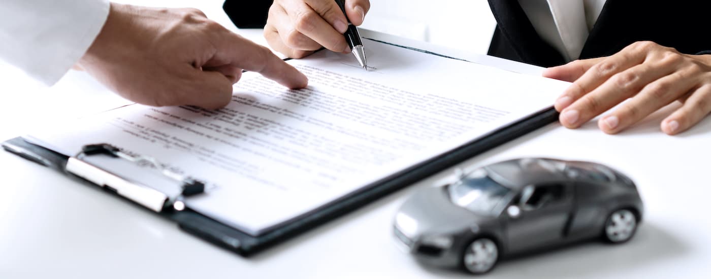 Man signing paperwork on a black clipboard for used car financing
