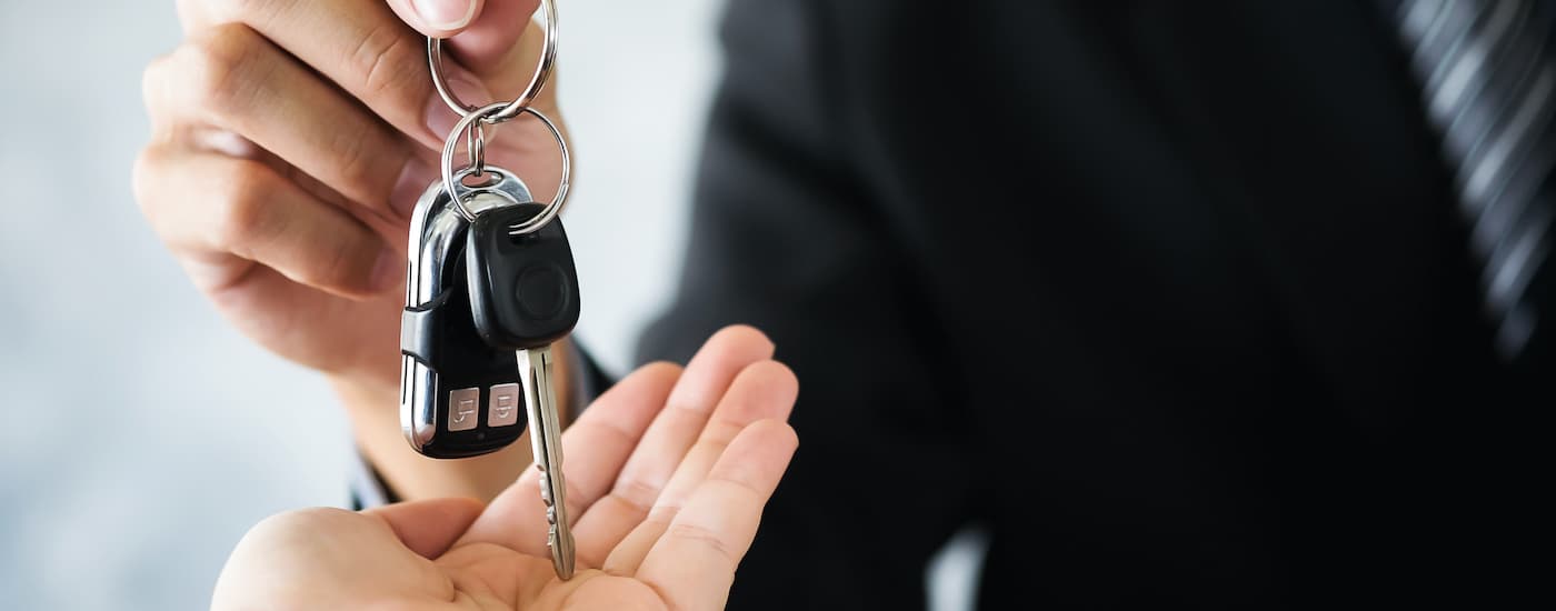 Salesman in a black suit handing car keys to a customer