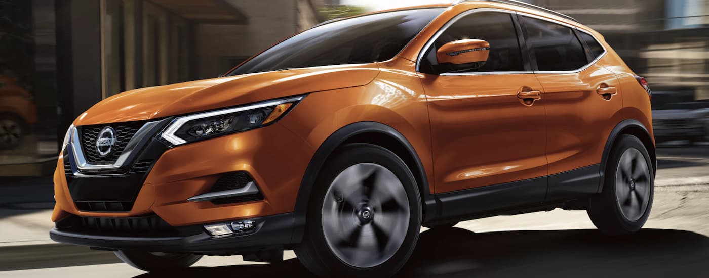 Closeup side view of an orange 2022 Nissan Rogue Sport rounding a city corner