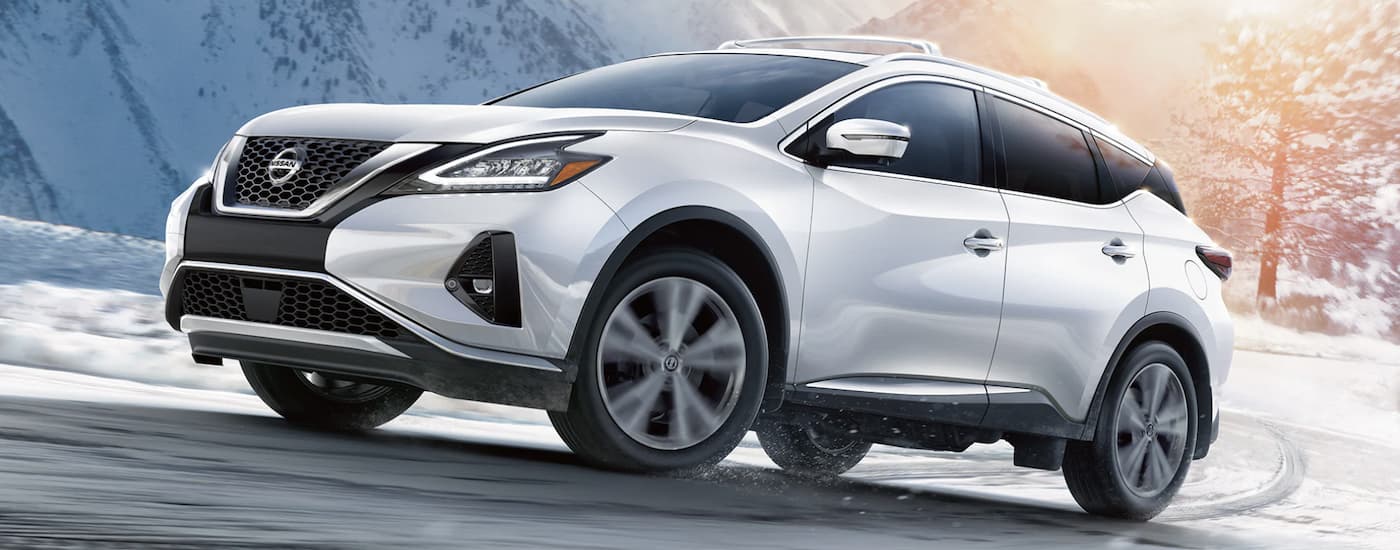 A white 2022 Nissan Murano driving uphill around a corner on a snowy road